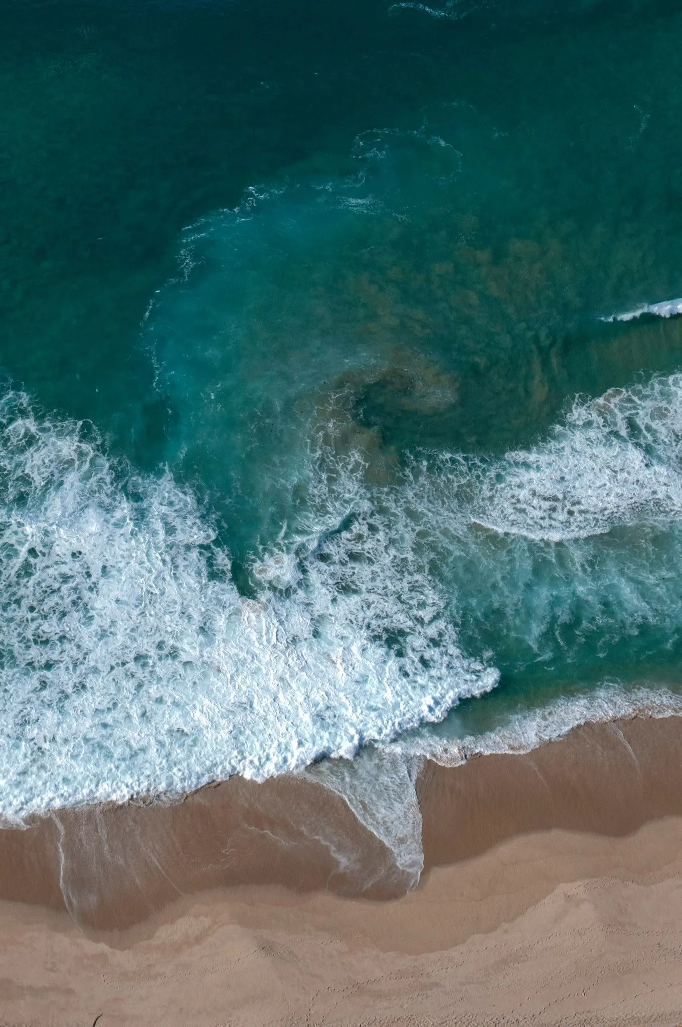 Top-down aerial photograph of waves breaking along the shoreline